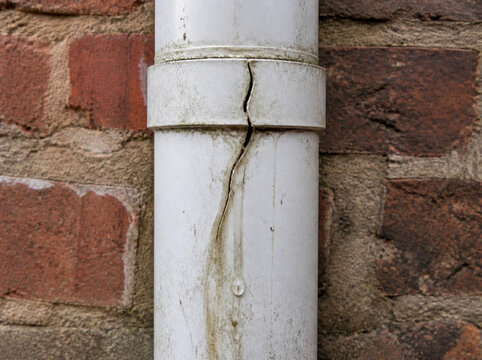 Plastic drain pipe with a major structural crack and leakage running down the brick wall