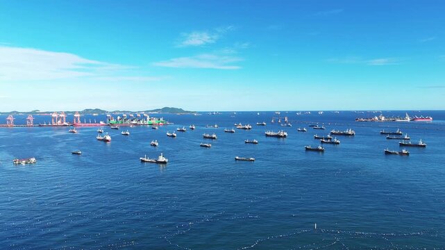 Fleet of oil tanker ships and commercial cargo vessels anchored in the deep blue sea near a long bridge. Global maritime logistics, international shipping trade, and energy transport.	