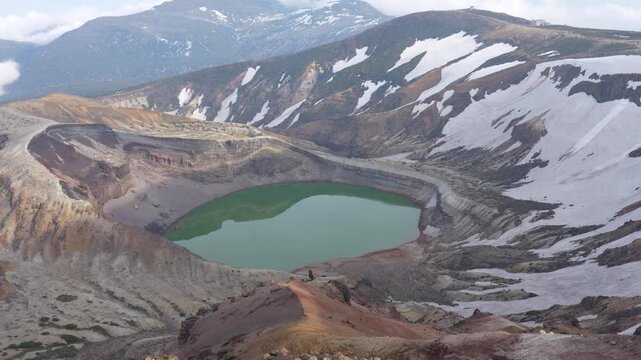 Blue mountain lake surrounded by green slopes and lingering snow in Japan