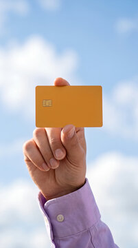 Hand holding blank orange payment card up to the sky
