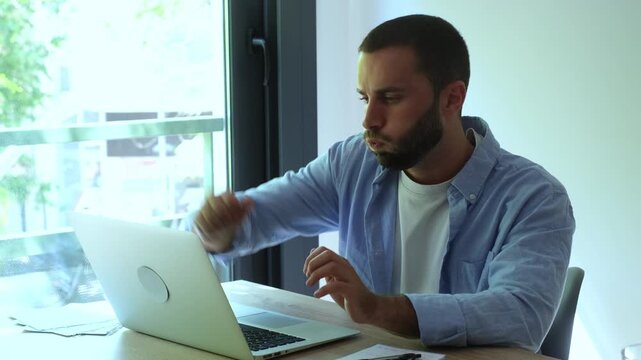 Young stressed male entrepreneur feeling angry and tired after receiving bad news or making a mistake, closing his laptop and thinking about the difficult financial problem at his desk