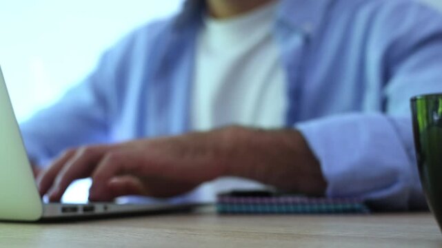 Close-up of a stressed male worker clenching his fist in anger and frustration while typing on his laptop computer, experiencing problems with work, deadlines, or technology issues
