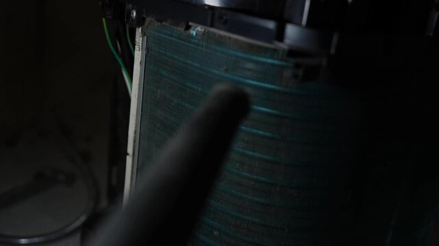 Close view of a dusty air conditioner coil in a dark indoor space with a cleaning tool in the foreground, Air conditioner coil cleaning closeup