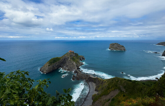 serene rocky coastline with lighthouse and ocean waves under cloudy sky, aerial view from high vantage point, still scene of natural beauty and travel destination, blue and green hues, cool.