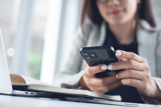 Young asian business woman using mobile phone while working on laptop computer in office. 