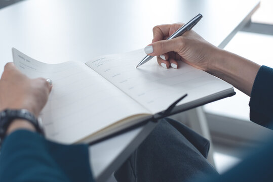 Business woman planning work event, hand writing on weekly schedule notebook, close up. Business event planning, timetable agenda plan