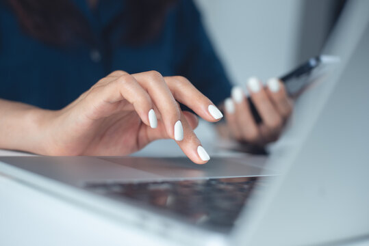 Close up, business woman using laptop surfing the net and holding smartphone during working in modern office