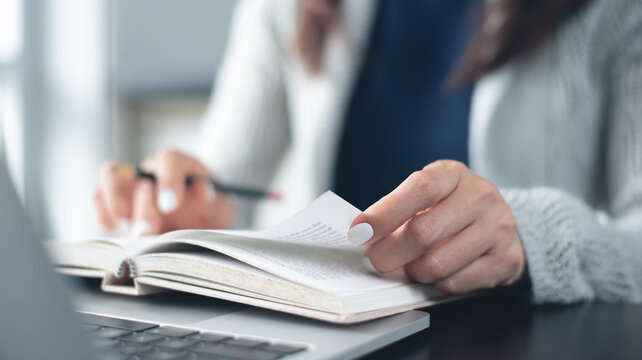 Woman reading a book with laptop computer on office desk, close up