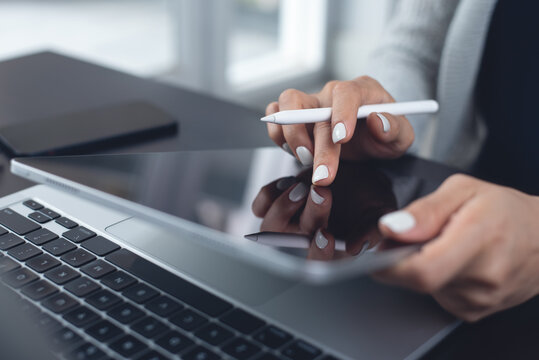 Close up, business woman using stylus pen and digital tablet with on laptop on office desk, proofreading e-document, corporate business concept