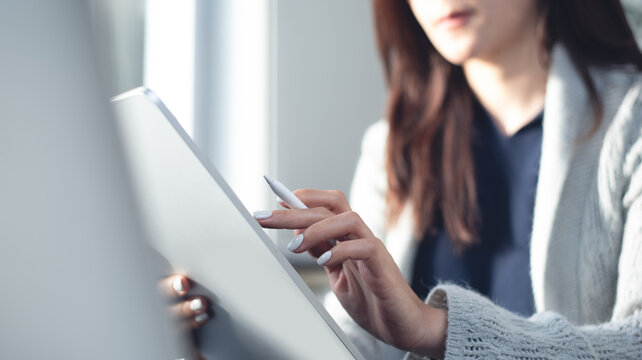 Asian business woman using digital tablet working at home office with laptop computer on desk in natural light, close up