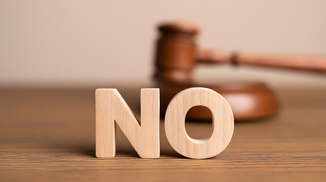 Wooden letters spelling the word no stand on a table with a judge gavel in the background, representing legal denial and court verdict