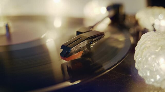 Close up of a stylus playing a vinyl record on a vintage turntable during a relaxing evening. Warm string lights create a cozy atmosphere around the classic audio equipment.