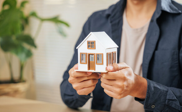 Real estate agent holds a miniature house model, representing property, finance, home loans, and housing concepts