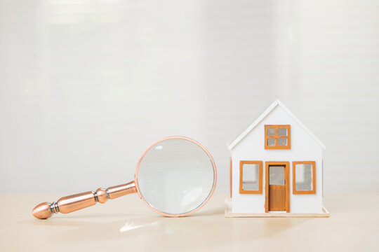 Magnifying glass with a white house model represents property search and finance. Focus on loans, inspection, and real estate to secure the best mortgage