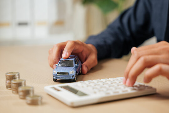 A person uses a calculator near coins and a car model, calculating auto loan payments and taxes. Perfect for car sales, finance, insurance