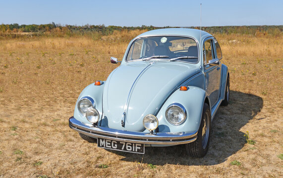 Classic light blue Volkswagen Beetle parked in a grassy field
