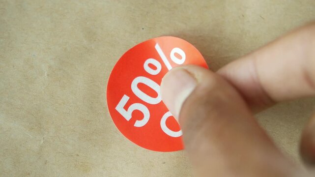 Close up shot of hand placing 50% off sticker on a brown paper bag, showing a special offer and discount promotion