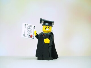 Obraz premium Indonesia - November 24, 2025 : Mini toy of action figure at table with blurred background. Miniature photography concept design. Minifigure of student with graduation gown, cap and certificate.
