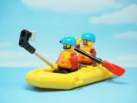 Indonesia - May 10, 2023 : Mini toy of action figure at table with blur background. Miniature photography concept design. Minifigure of people character with inflatable rubber boat and selfie camera.