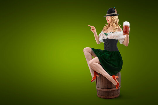 Oktoberfest girl sitting on a wooden barrel, waitress pointing arm at empty copy space. Woman in dirndl, tyrolean hat serving big beer mugs on isolated background. Traditional party, autumn festival.