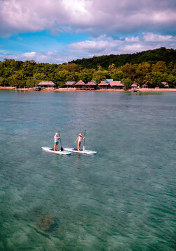 View of couple of tourist are enjoy on water sport paddle sup-board with kayaking along at the edge of the sea beach under crystal clear of water in the island of summer trip