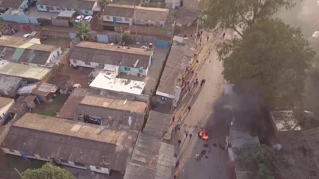 Aerial view of a street with small structures and people, with a small fire burning on the road.