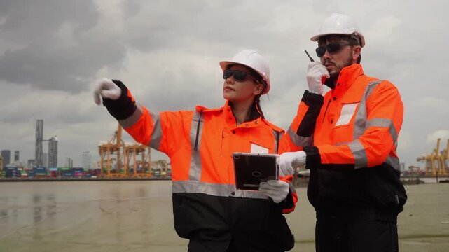 Port engineers pointing and using walkie talkie at shipping terminal, Logistics managers team with tablet discussing cargo port operations, Workers collaborating outdoors at container harbor