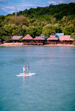 View of couple of tourist are enjoy on water sport paddle sup-board with kayaking along at the edge of the sea beach under crystal clear of water in the island of summer trip