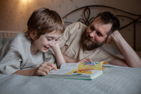 Father and son reading book together lying on bed at home. Bond between father and son, parenting, quality time, education, love, childhood development, family connection.