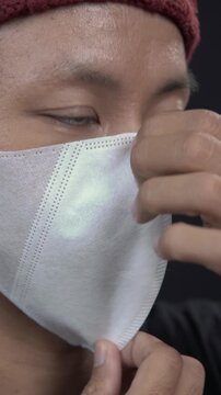 Close up of Asian man wearing white protective face mask for healthcare prevention against virus and pollution on dark background.