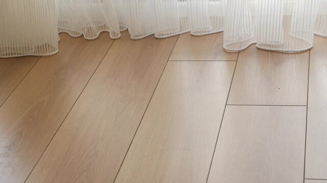 A vacuum cleaner head moving back and forth on a light brown wooden floor cleaning dust under a white transparent curtain, household chores dynamic footage