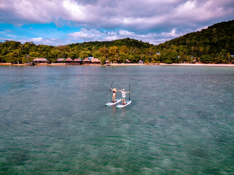 View of couple of tourist are enjoy on water sport paddle sup-board with kayaking along at the edge of the sea beach under crystal clear of water in the island of summer trip