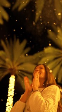 Smiling woman reaching toward snowy Christmas-lit palm trees