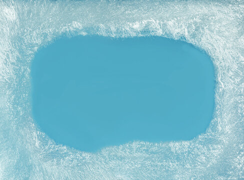 Blue icy frost texture background with dense frozen winter patterns on glass window with an empty blue space in the middle for seasonal backgrounds.