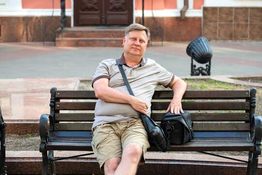 mature blond man sits happily on a park bench, enjoying rest and fresh air during the day.