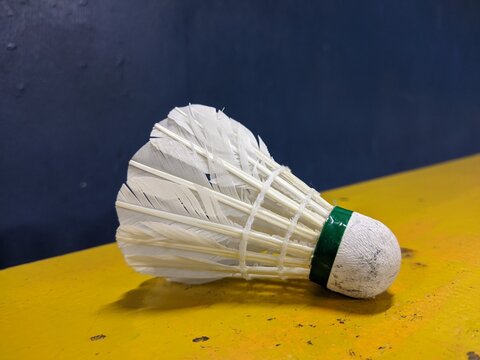 Close-up of a Single White Feather Badminton Shuttlecock Lying on Yellow Surface with Dark Blue Background