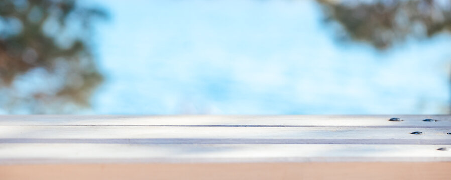 Close-up view of a wooden deck with a blurred blue water background, sunlight reflecting off the surface, creating a serene outdoor atmosphere