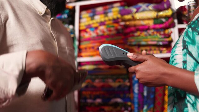 African woman small business owner accepting customer's contactless payment with a pos terminal in her shop