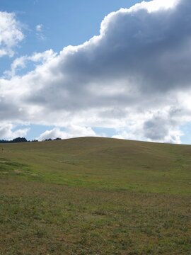 Rolling Grassy Hill Beneath Large White and Gray Clouds in a Blue Sky