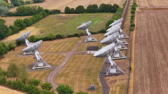 Multiple Radio Telescopes Arranged in a Line Within a Dry Grassy Field During a Bright Summer Day
