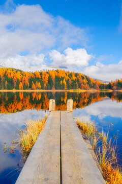 Vertical photo. Lake and a small pier. Autumn landscape. Clouds and fall forest. Incredible view of the mountain valley with lake. Background, wallpaper, postcards