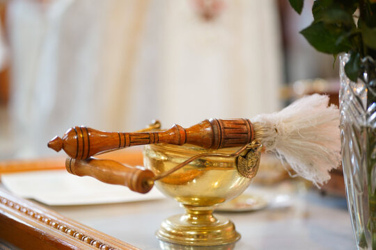 Wooden aspergillum rests above a vessel of holy water, prepared for use during a church service and baptismal ritual.