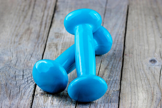 Pair of small blue vinyl dumbbells resting on a weathered wooden surface, ideal for concepts of home exercise, strength training, wellness, gym equipment, and healthy lifestyle