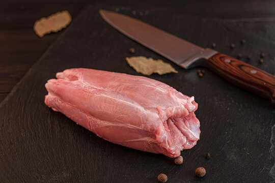 Fresh raw pork meat cuts with bay leaves and peppercorns on dark wooden board
