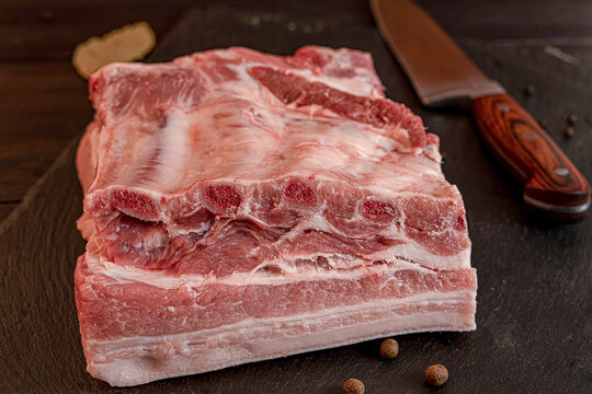 Fresh raw pork meat cuts with bay leaves and peppercorns on dark wooden board