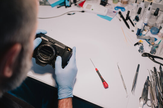 Technician in protective gloves inspecting a mirrorless camera body at a professional repair workbench with precision tools for maintenance and technical service