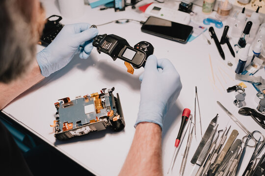 Technician examining a disassembled digital camera with exposed internal components at a repair bench, showing precision servicing, hardware access and repairability