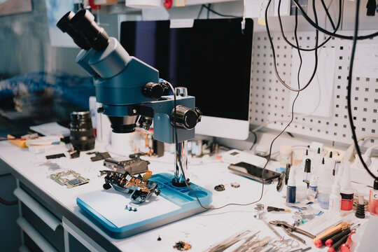 Specialized electronics and camera repair workstation with stereo microscope, disassembled components and precision tools prepared for professional diagnostics and servicing