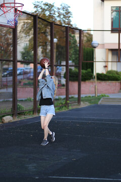 Blonde woman in jeans and denim shorts shooting a basketball on an outdoor court