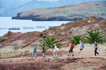 Group of hikers follows coastal trail beside offshore aquaculture pens at Sao Lourenco, Madeira....